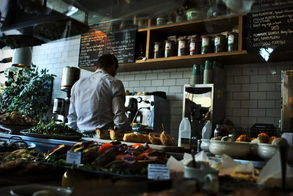 A café counter with a barista working behind a display of food